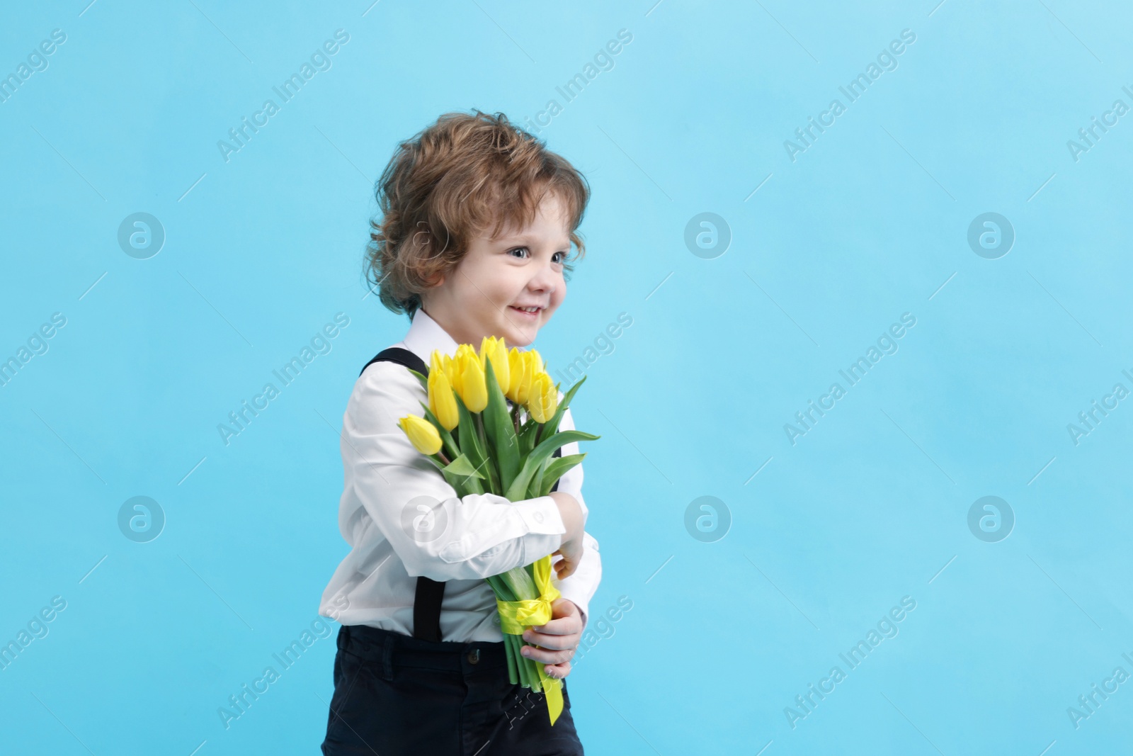 Photo of Cute little boy with bouquet of tulips on light blue background. Space for text