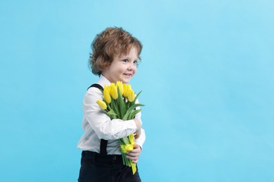 Photo of Cute little boy with bouquet of tulips on light blue background. Space for text