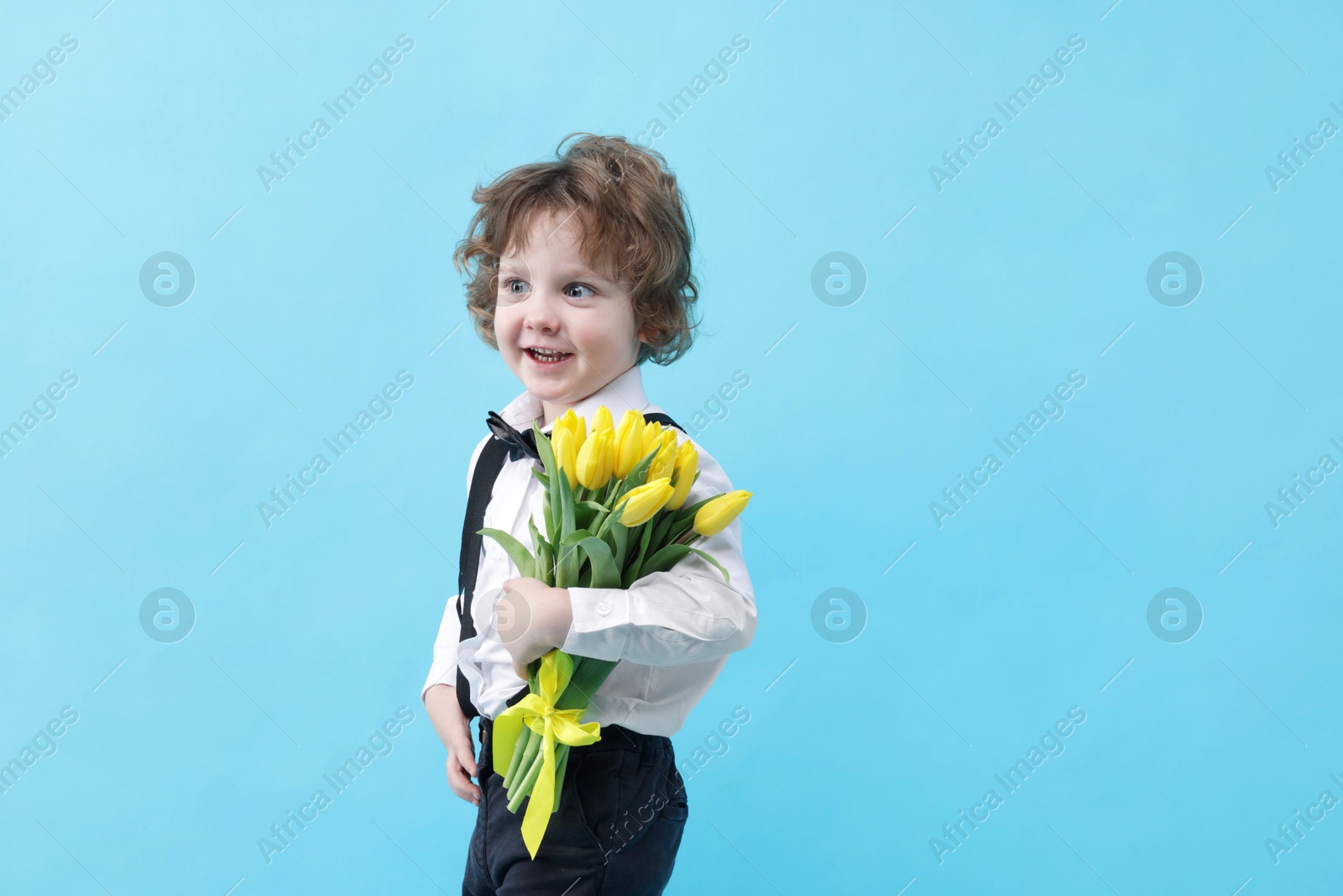 Photo of Cute little boy with bouquet of tulips on light blue background. Space for text