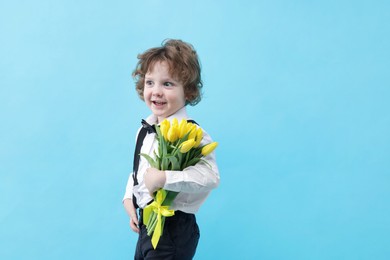 Photo of Cute little boy with bouquet of tulips on light blue background. Space for text