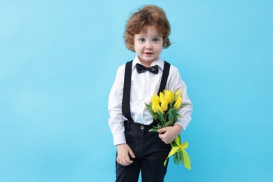 Photo of Cute little boy with bouquet of tulips on light blue background