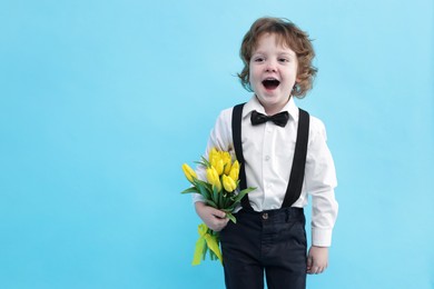 Photo of Cute little boy with bouquet of tulips on light blue background. Space for text