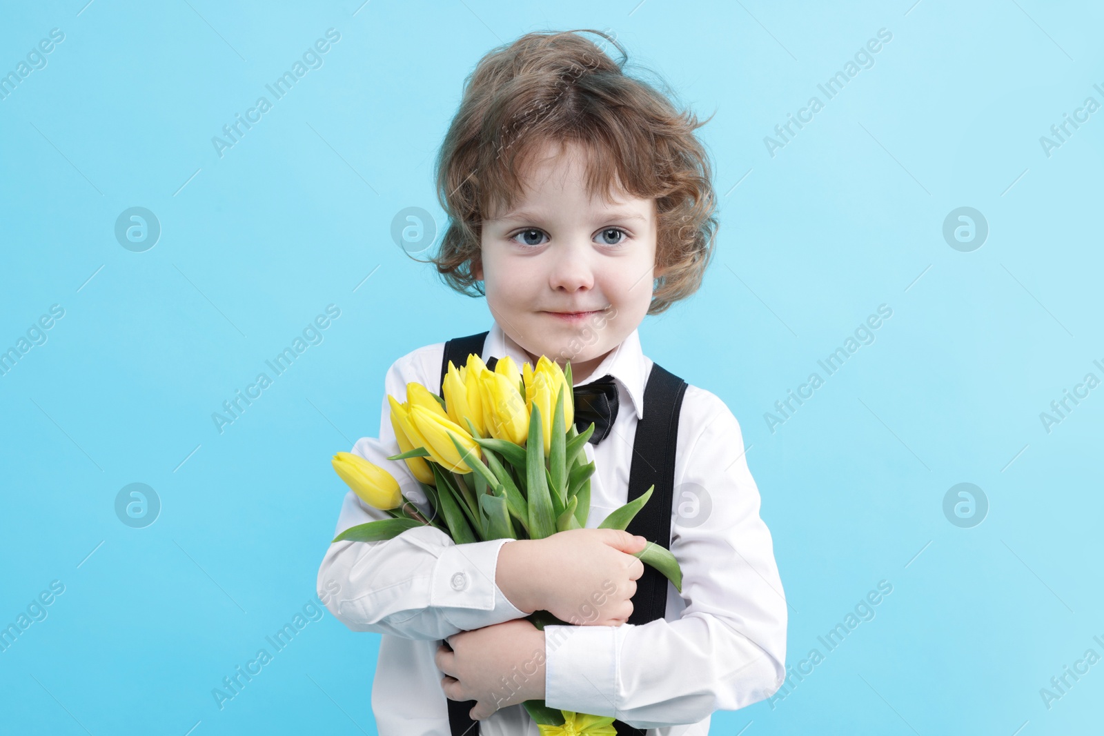 Photo of Cute little boy with bouquet of tulips on light blue background