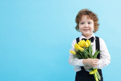 Photo of Cute little boy with bouquet of tulips on light blue background. Space for text