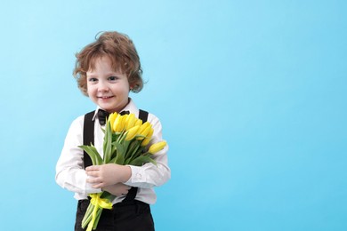 Photo of Cute little boy with bouquet of tulips on light blue background. Space for text