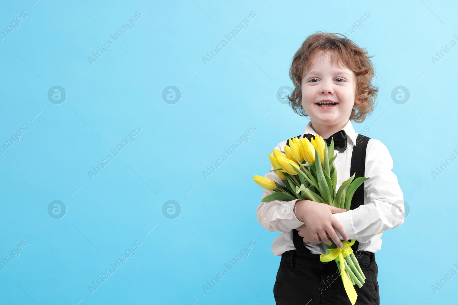 Photo of Cute little boy with bouquet of tulips on light blue background. Space for text