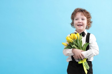 Photo of Cute little boy with bouquet of tulips on light blue background. Space for text