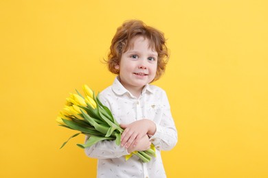 Cute little boy with bouquet of tulips on yellow background