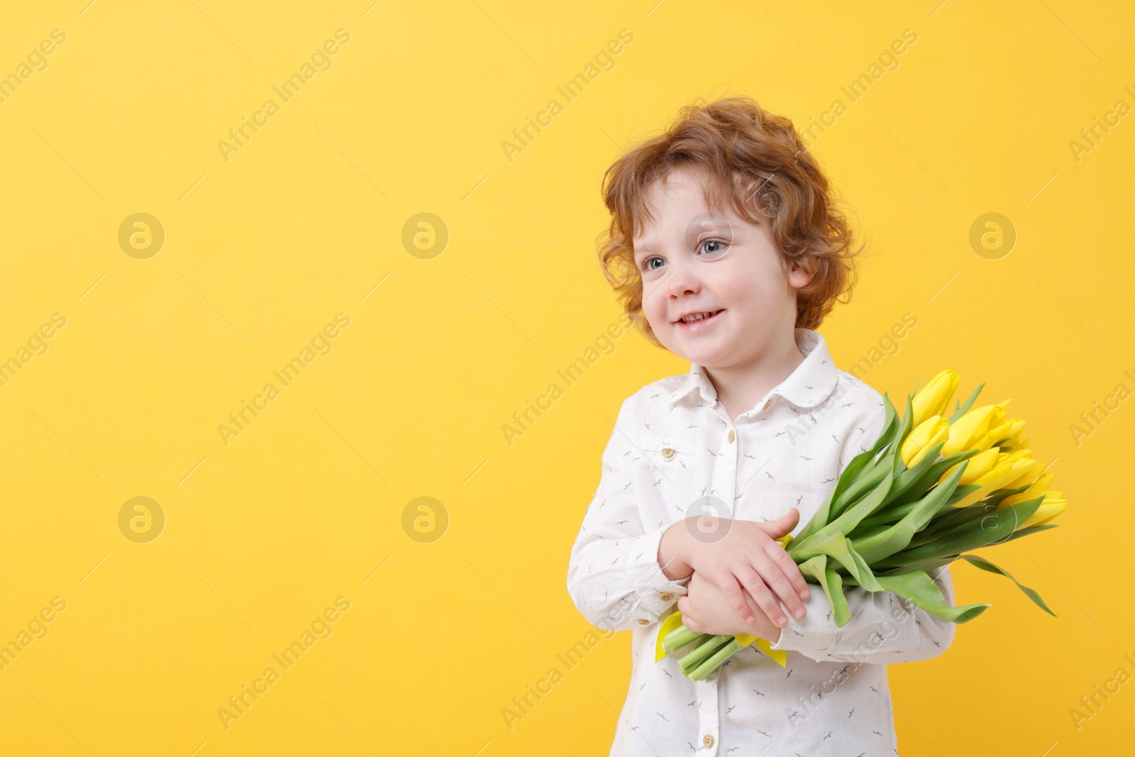 Photo of Cute little boy with bouquet of tulips on yellow background. Space for text