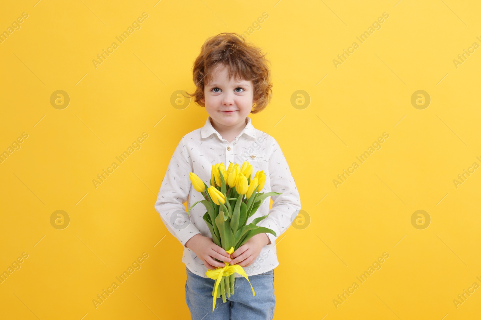 Photo of Cute little boy with bouquet of tulips on yellow background