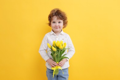 Cute little boy with bouquet of tulips on yellow background