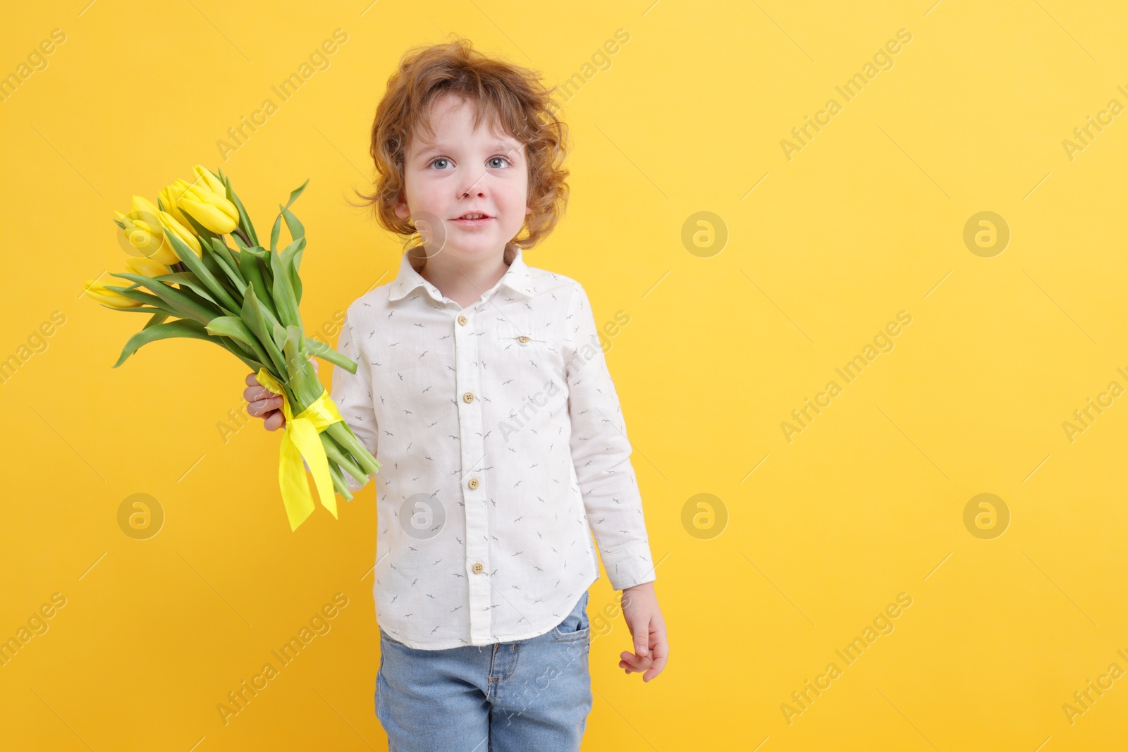 Photo of Cute little boy with bouquet of tulips on yellow background. Space for text