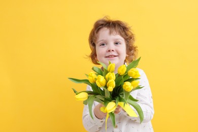 Cute little boy with bouquet of tulips on yellow background. Space for text