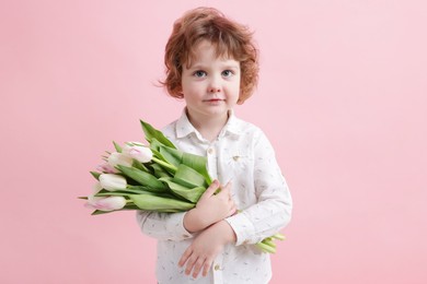 Cute little boy with bouquet of tulips on light pink background