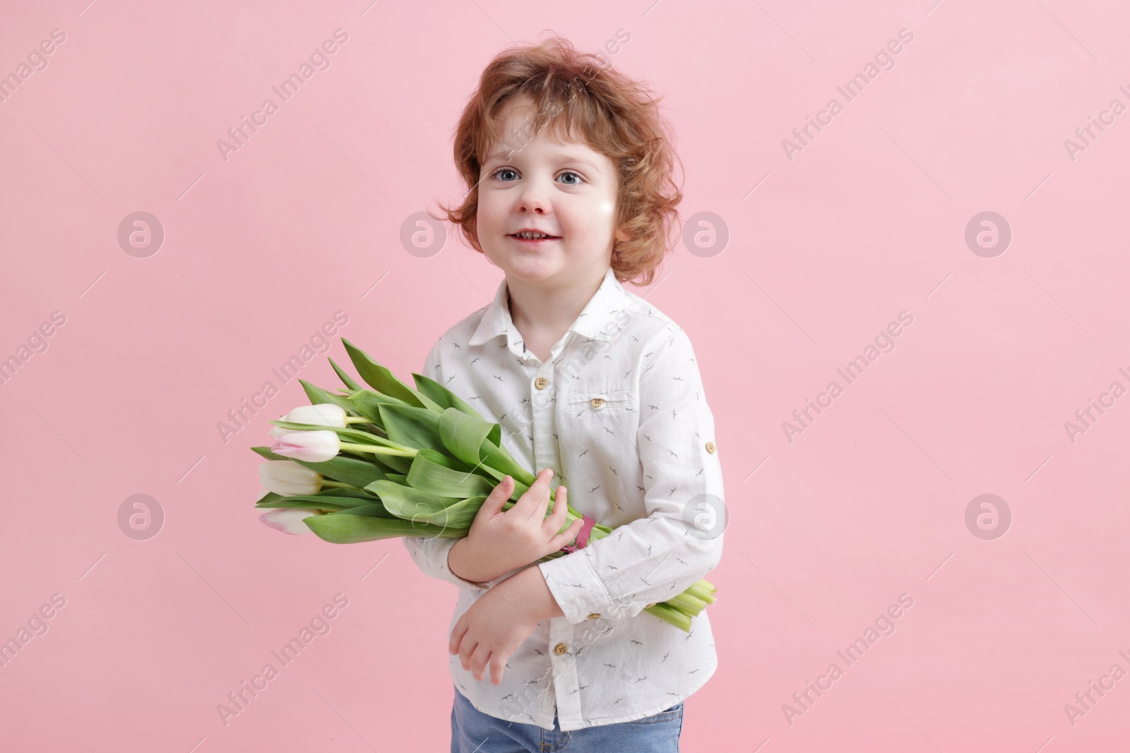 Photo of Cute little boy with bouquet of tulips on light pink background