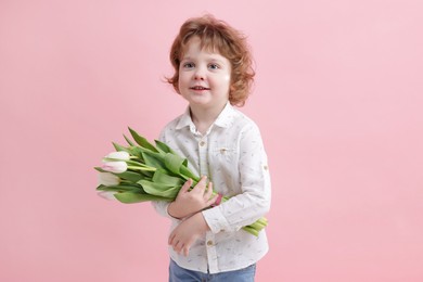 Photo of Cute little boy with bouquet of tulips on light pink background