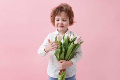 Photo of Cute little boy with bouquet of tulips on light pink background