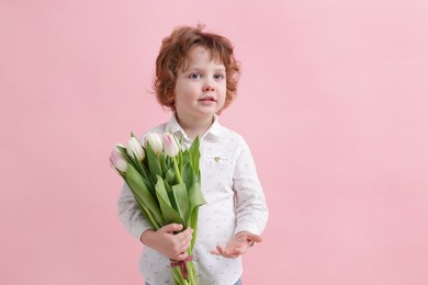 Cute little boy with bouquet of tulips on light pink background