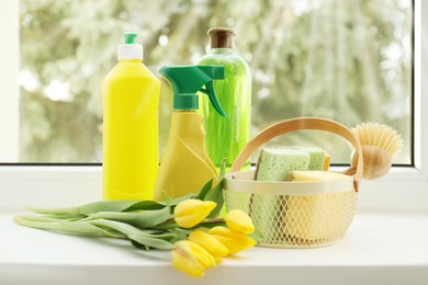 Photo of Spring cleaning. Detergents, supplies and tulips on windowsill indoors