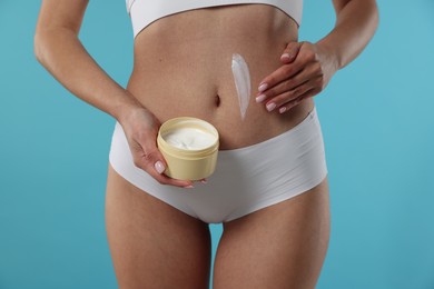 Photo of Woman applying anti cellulite cream on light blue background, closeup