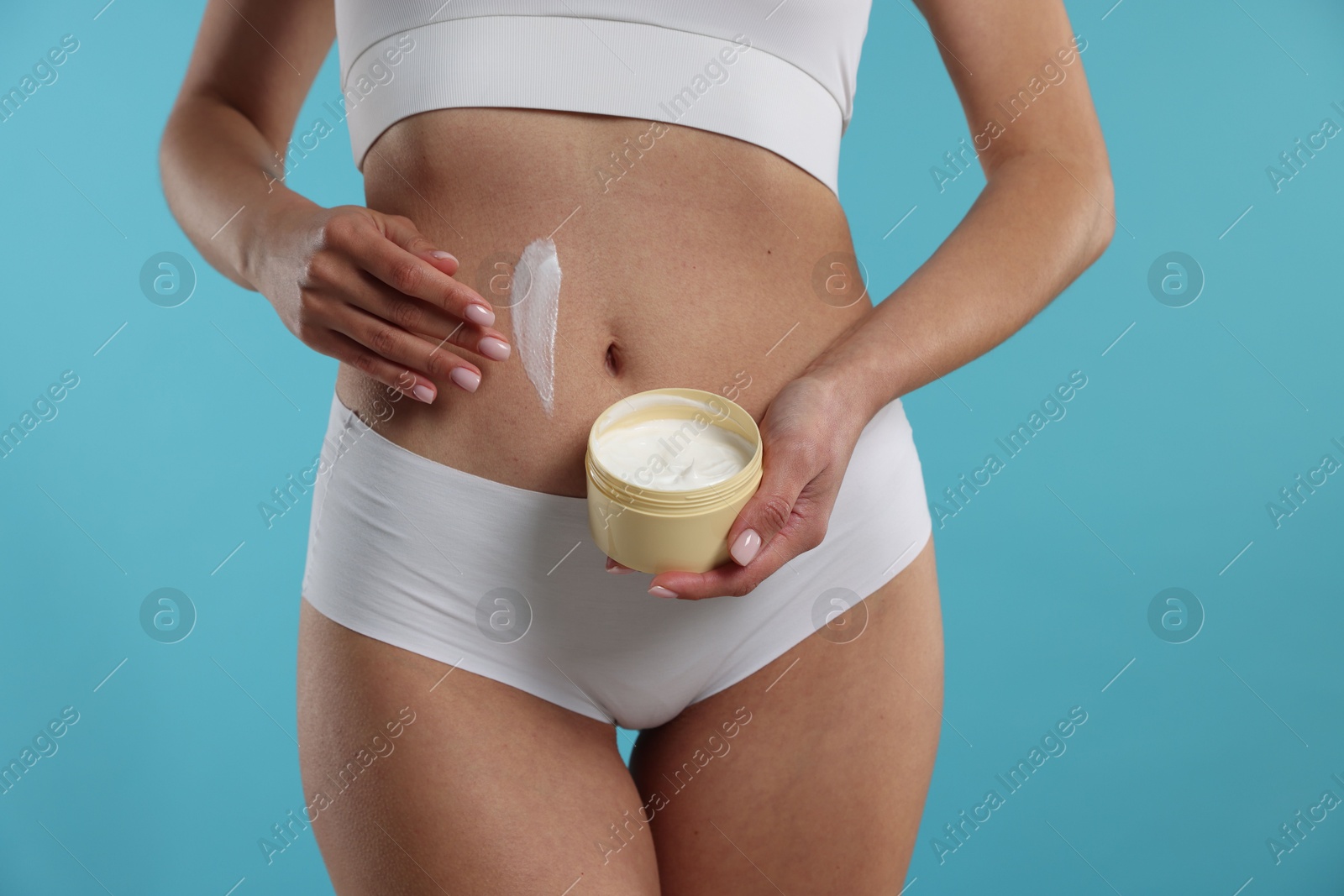 Photo of Woman applying anti cellulite cream on light blue background, closeup