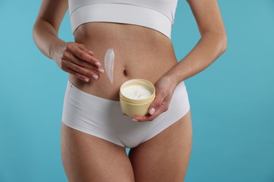 Photo of Woman applying anti cellulite cream on light blue background, closeup