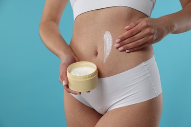 Photo of Woman applying anti cellulite cream on light blue background, closeup