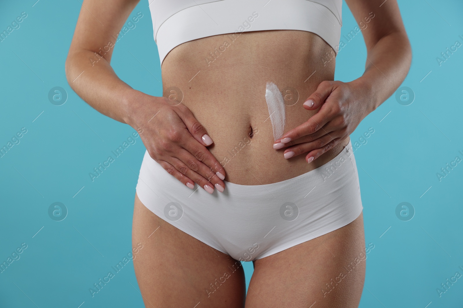 Photo of Woman applying anti cellulite cream on light blue background, closeup