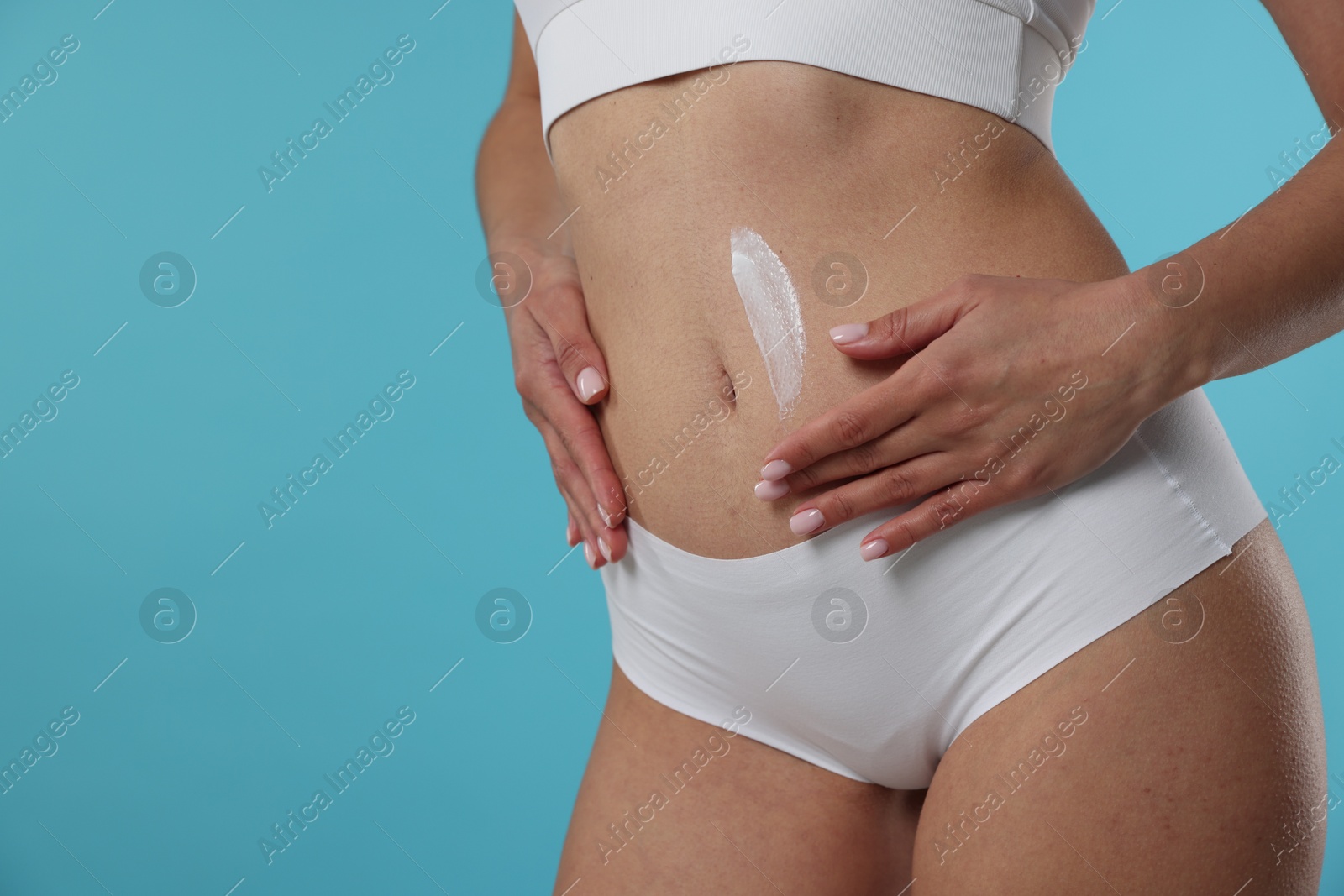 Photo of Woman applying anti cellulite cream on light blue background, closeup. Space for text