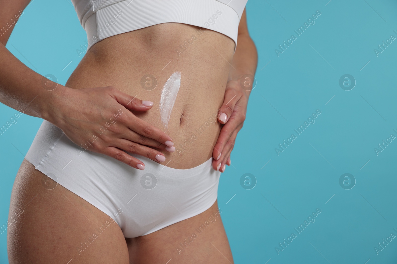 Photo of Woman applying anti cellulite cream on light blue background, closeup. Space for text