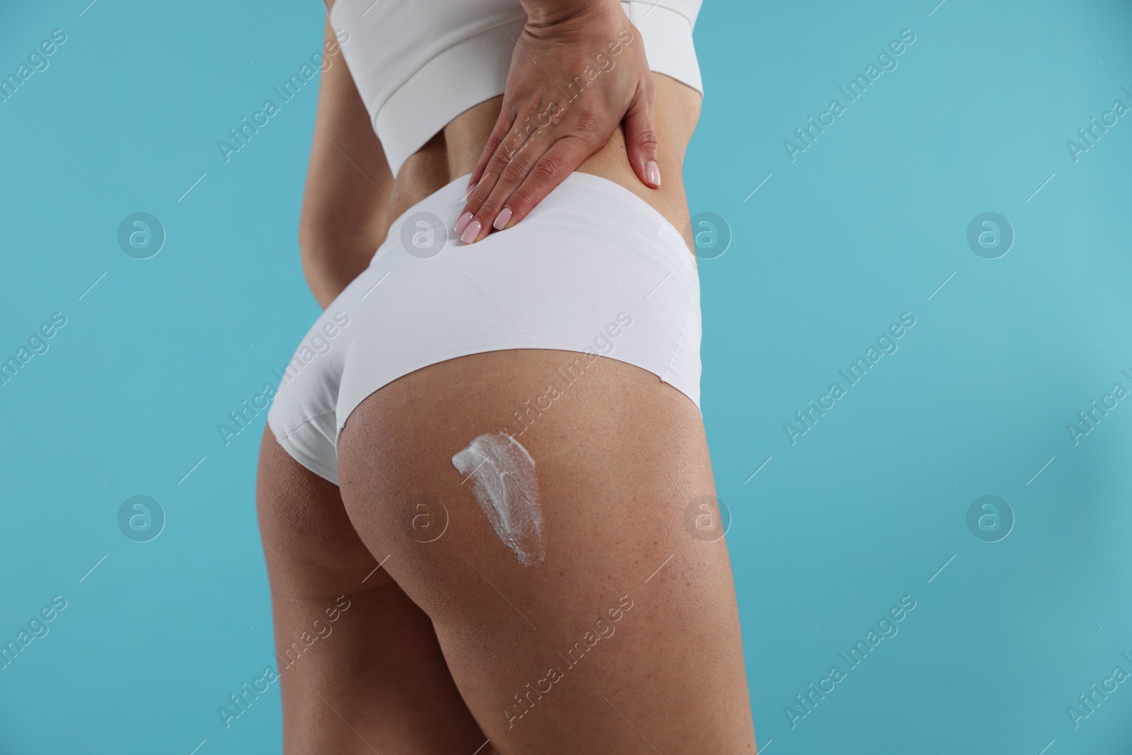 Photo of Woman applying anti cellulite cream on light blue background, closeup