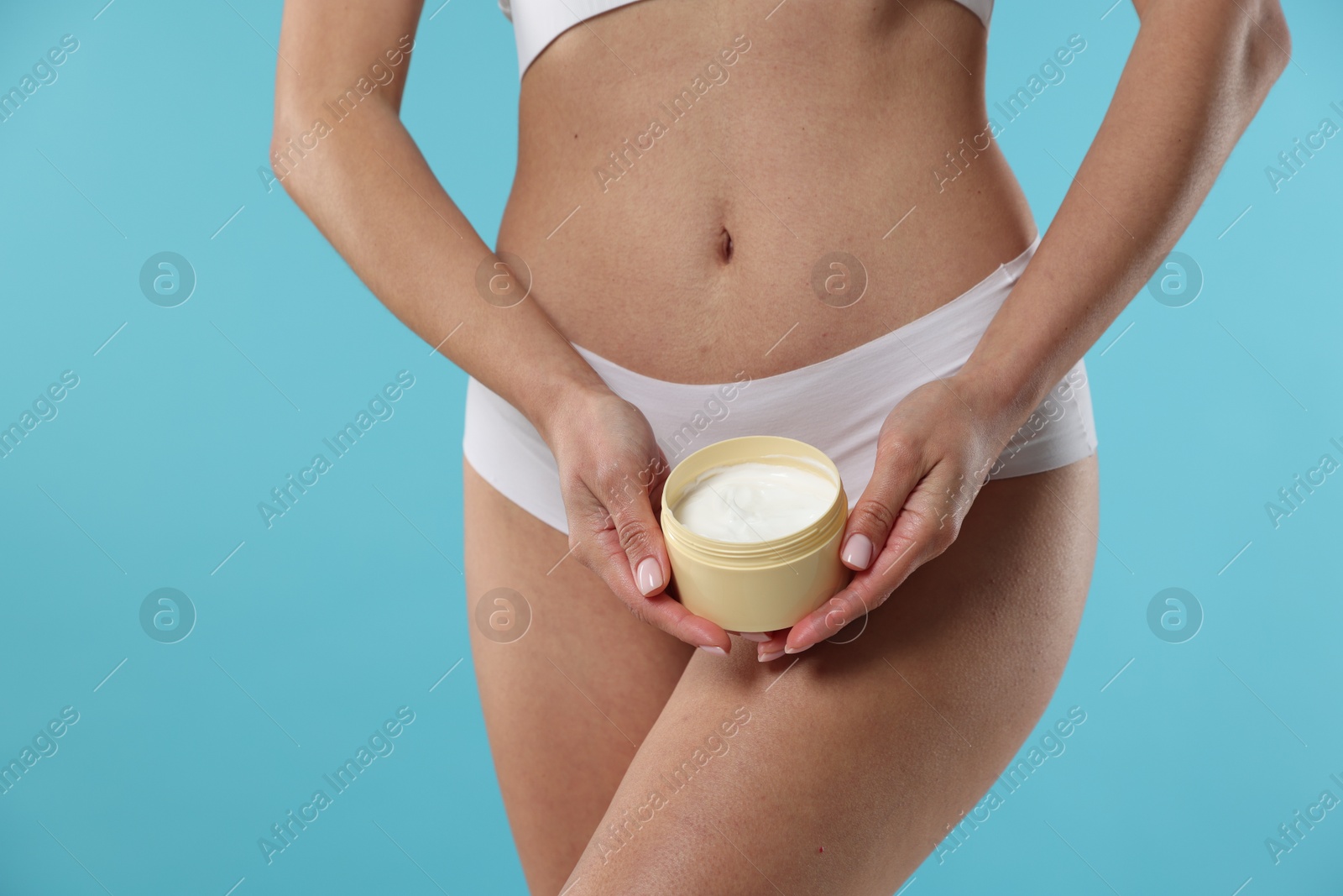 Photo of Woman with jar of anti cellulite cream on light blue background, closeup