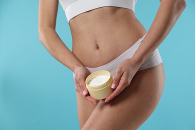 Woman with jar of anti cellulite cream on light blue background, closeup