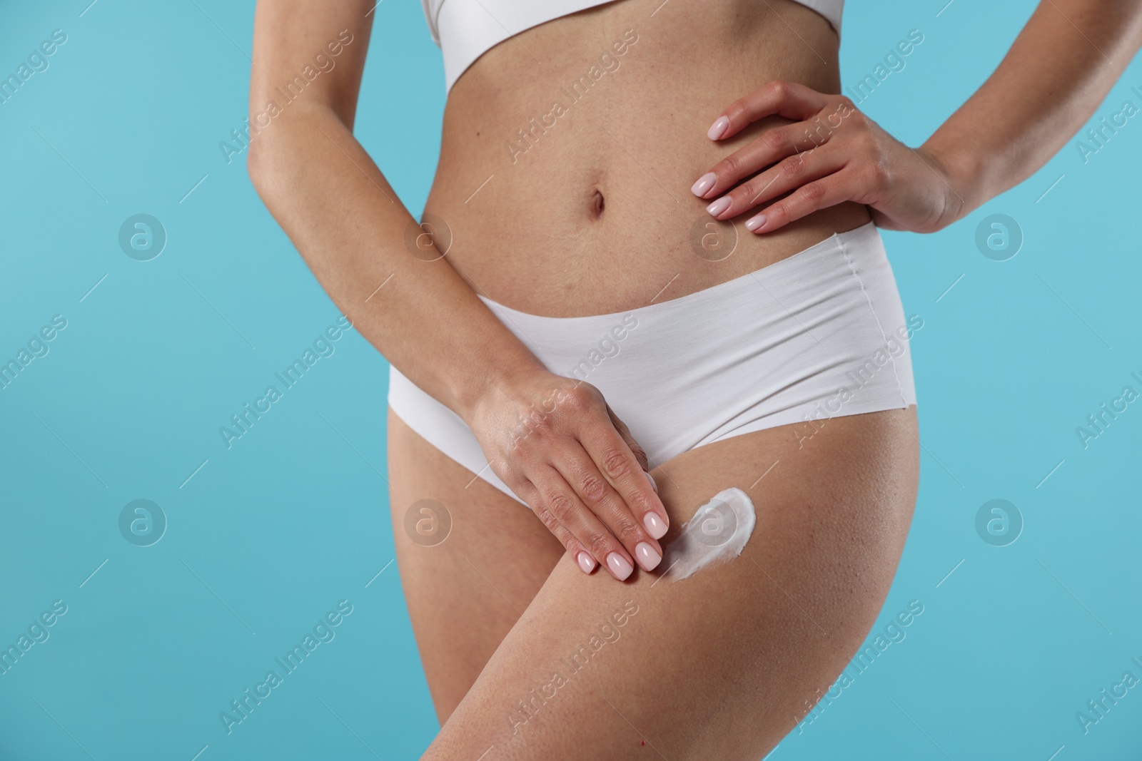 Photo of Woman applying anti cellulite cream on light blue background, closeup