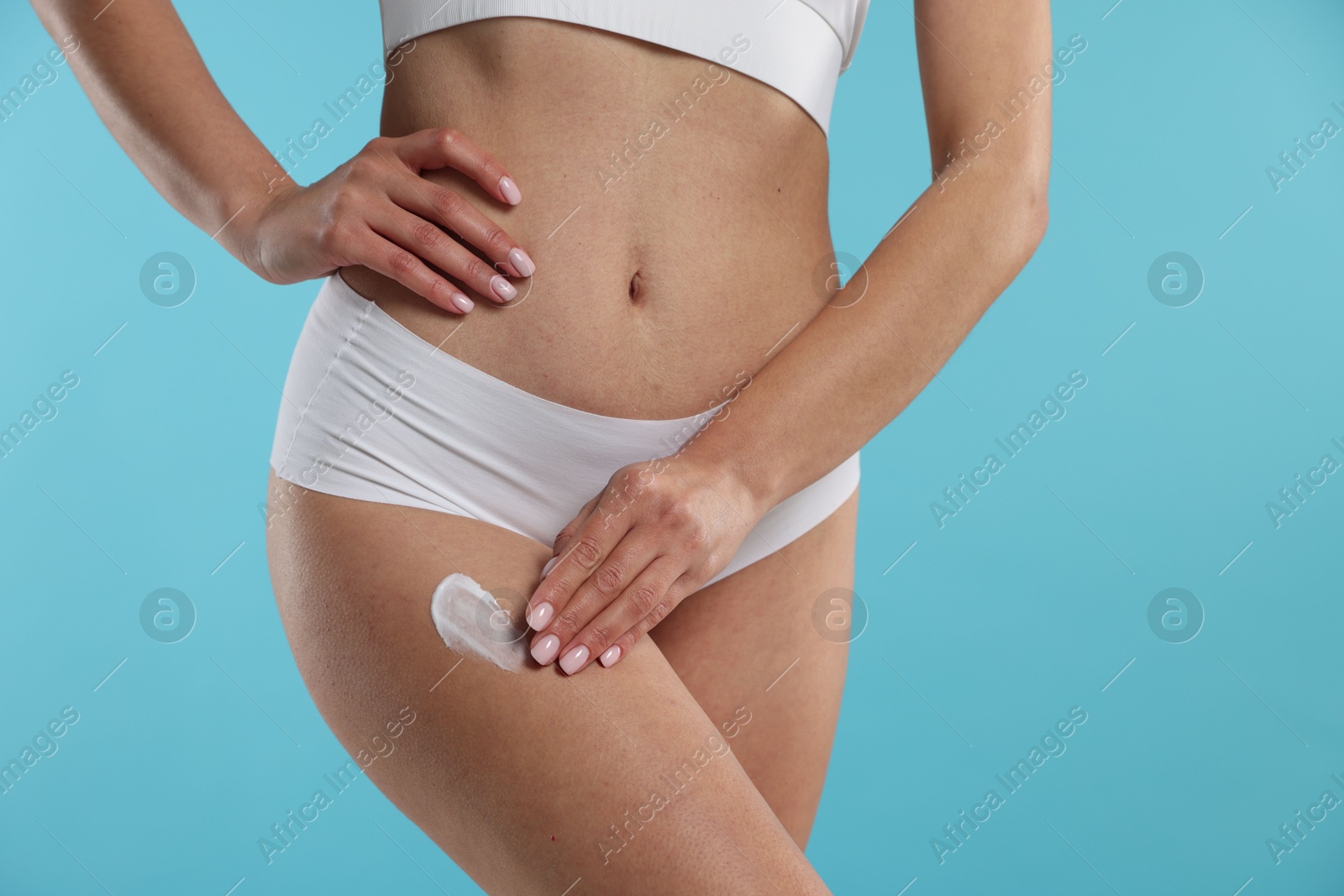 Photo of Woman applying anti cellulite cream on light blue background, closeup