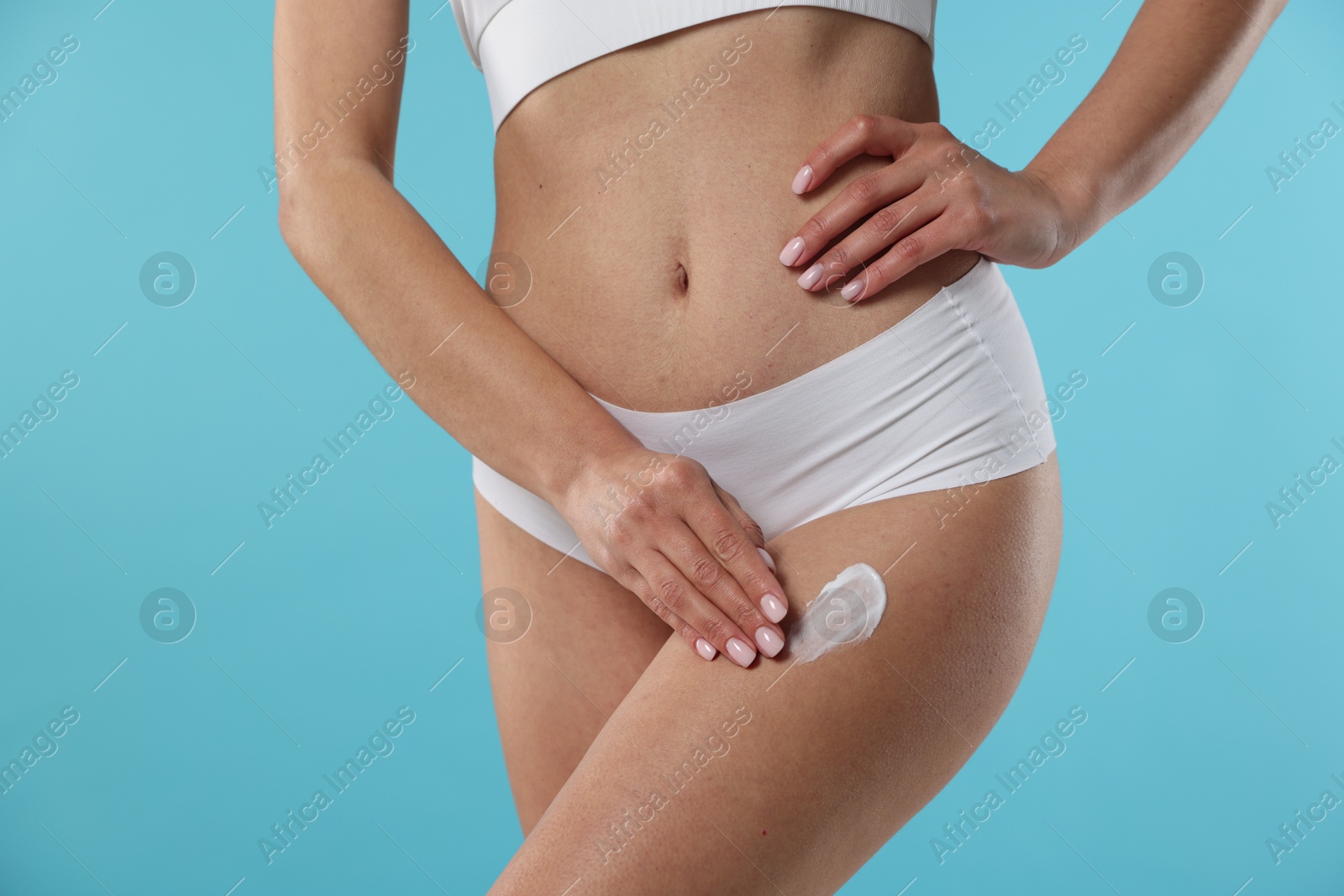 Photo of Woman applying anti cellulite cream on light blue background, closeup