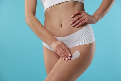 Woman applying anti cellulite cream on light blue background, closeup