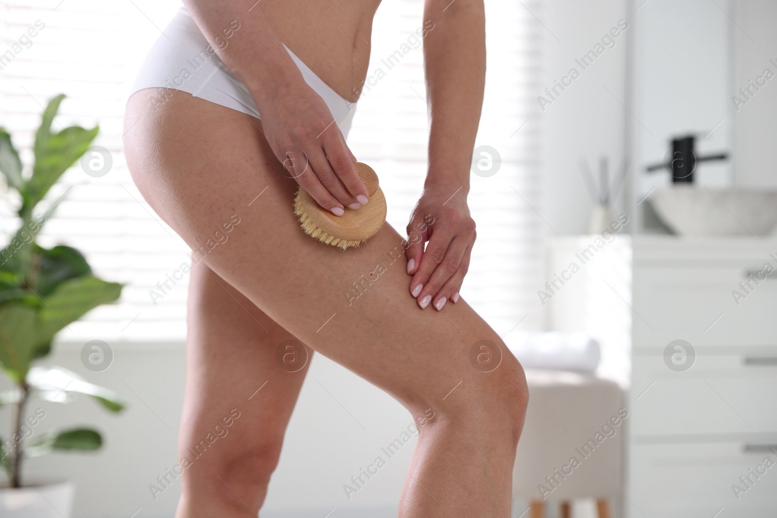 Photo of Woman doing anti cellulite massage with brush indoors, closeup