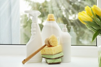 Photo of Spring cleaning. Detergents, supplies and tulips on windowsill indoors