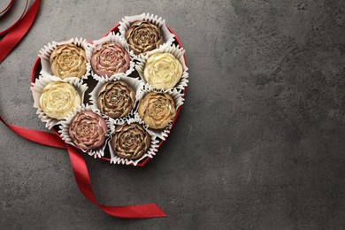 Photo of Flower shaped chocolate bonbons in box and red ribbon on grey table, top view. Space for text