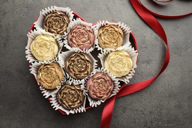 Photo of Flower shaped chocolate bonbons in box and red ribbon on grey table, top view