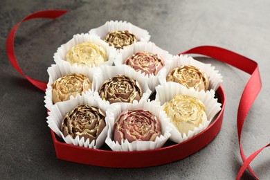 Photo of Flower shaped chocolate bonbons in box and red ribbon on grey table, closeup