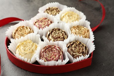 Photo of Flower shaped chocolate bonbons in box and red ribbon on grey table, closeup