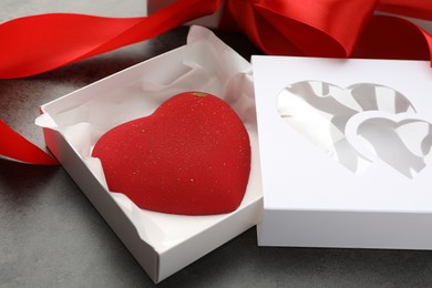 Photo of Heart shaped chocolate in box and red ribbon on grey table, closeup