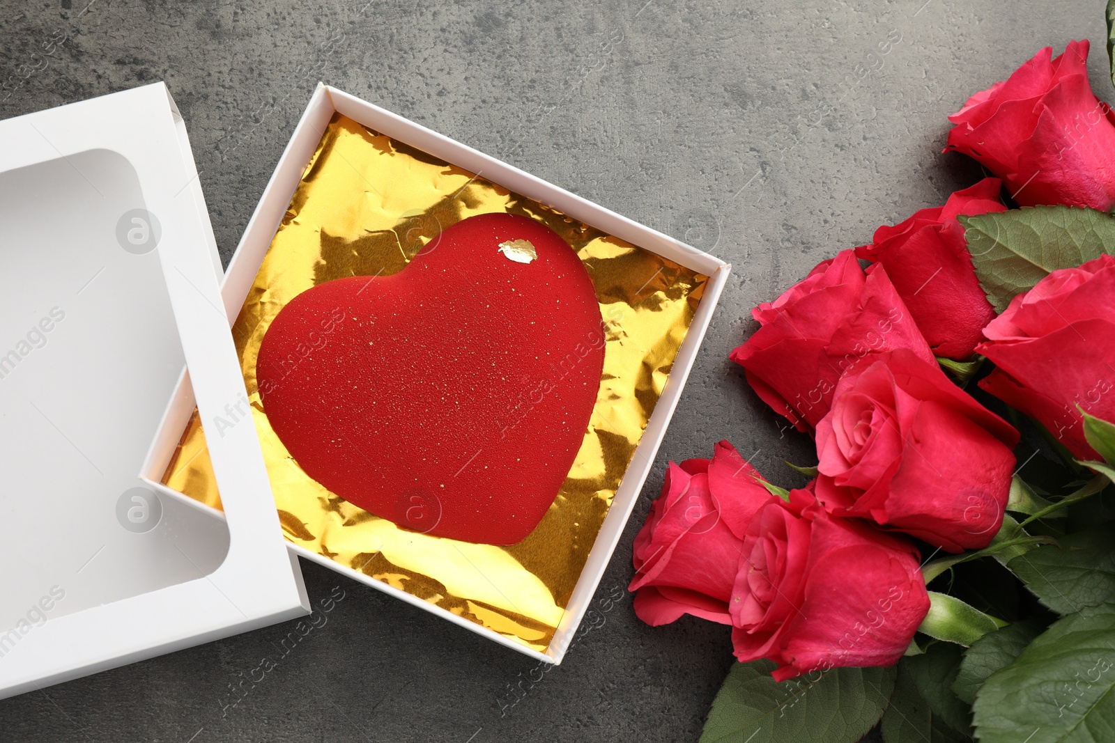 Photo of Heart shaped chocolate in box and red roses on grey table, flat lay