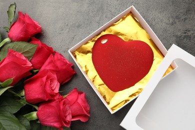 Photo of Heart shaped chocolate in box and red roses on grey table, flat lay