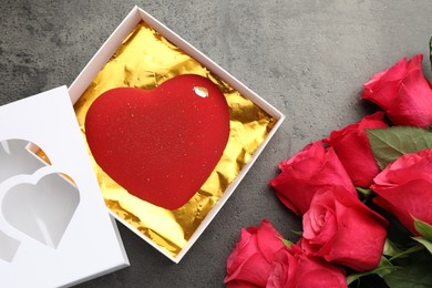 Photo of Heart shaped chocolate in box and red roses on grey table, flat lay