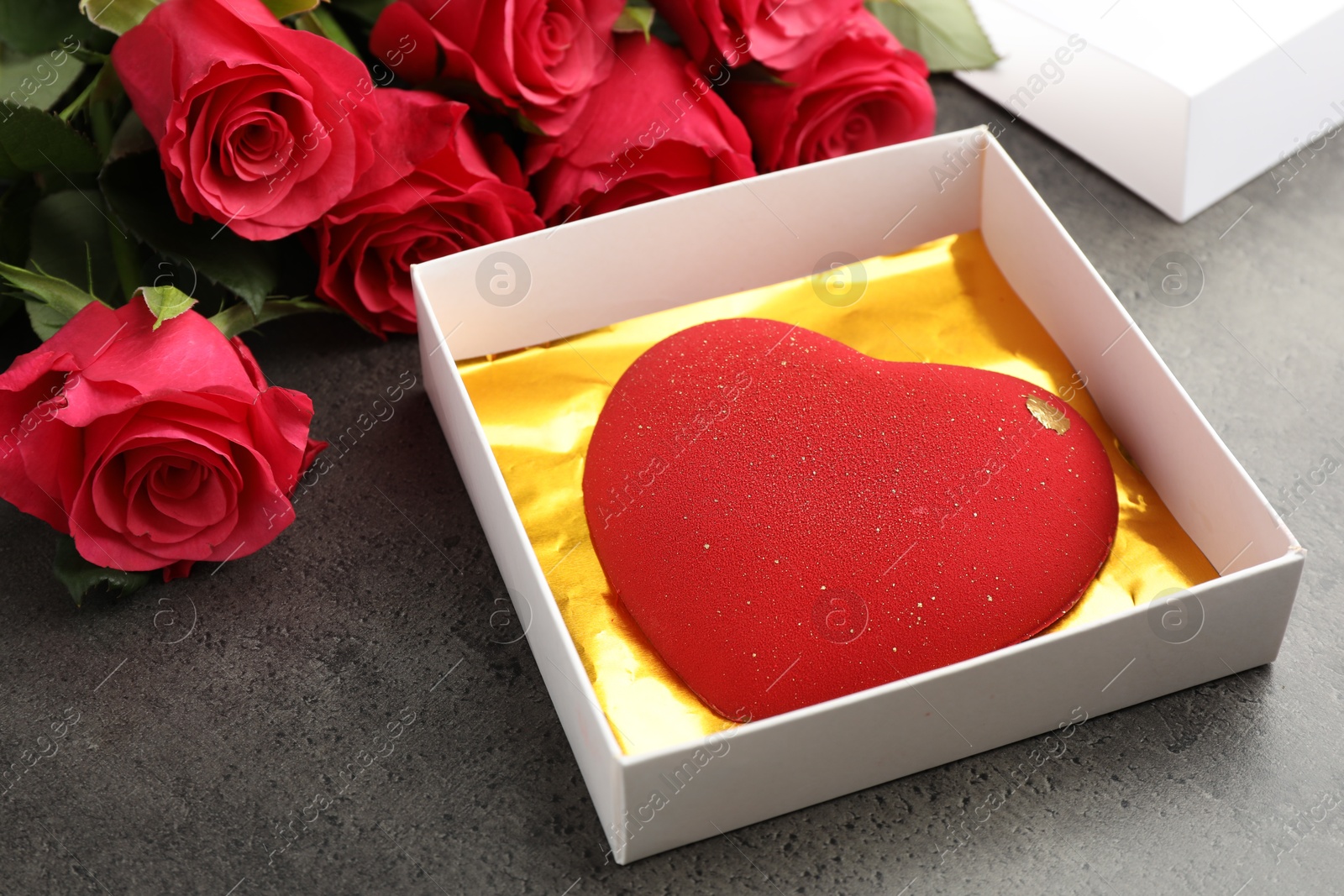 Photo of Heart shaped chocolate in box and red roses on grey table, closeup