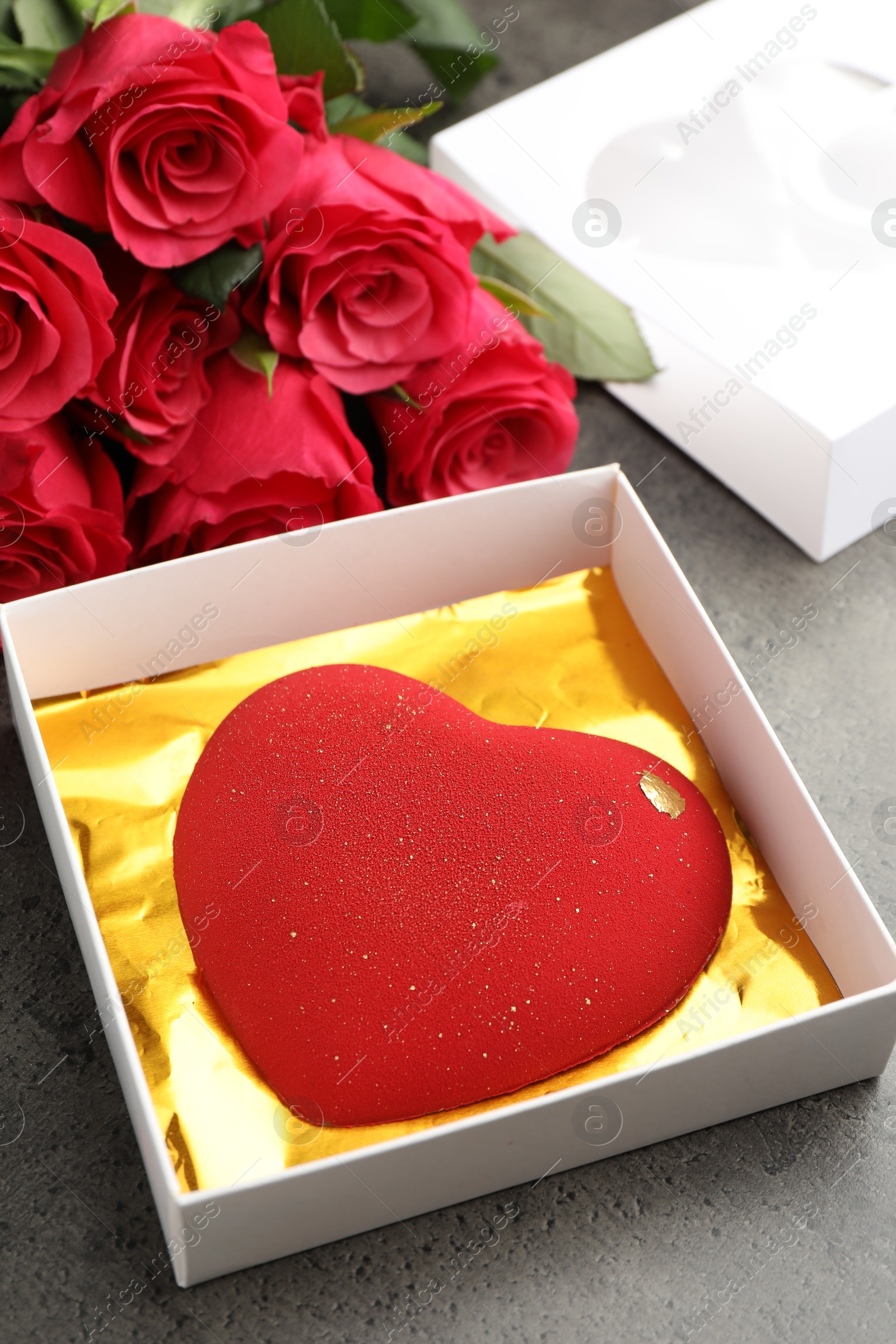 Photo of Heart shaped chocolate in box and red roses on grey table, closeup