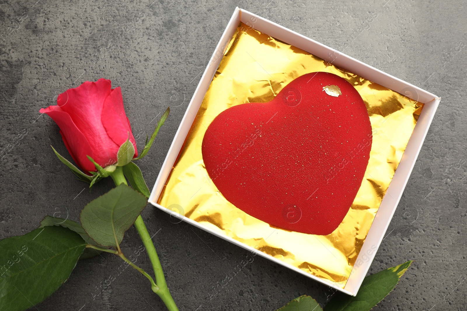 Photo of Heart shaped chocolate in box and red rose on grey table, flat lay